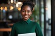 © Arfa_Media - Young black businesswoman smiling at the camera, confidently holding a laptop in a modern office environment, symbolizing professionalism, success, and digital productivity
