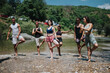 © qunica.com - Group of friends performs yoga poses along a sunny riverbank, showcasing balance and teamwork. Outdoor fitness scene highlights camaraderie and summer relaxation.