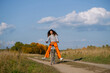 © wifesun - Young woman confidently balancing on a bicycle with feet off the pedals, expressing happiness and freedom while cycling a dirt track through a rural landscape surrounded by trees showing fall colors