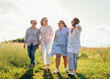 © Soloviova Liudmyla - Cheerful diverse women holding hand in hand walking through green grass meadow for woman friendship and happiness concept featuring four beautiful friends smiling in nature outdoor portrait area