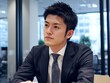 © Jumpei - オフィスで真剣な表情を浮かべながら仕事に向き合うスーツ姿の日本人ビジネスマン