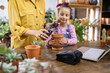© sofiko14 - A young girl learns how to pot a plant with her mother in a bright and inviting greenhouse setting