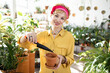 © sofiko14 - A woman in a yellow shirt and pink headscarf is gardening, filling a terracotta pot with soil