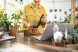 © sofiko14 - A woman is seen smiling as she plants a succulent in a pot, possibly following an online tutorial