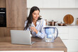 © Pixel-Shot - Young woman with water filter jug and laptop in kitchen