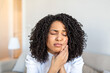 © Graphicroyalty - Pain in the tooth. Woman with toothache, People with dental-oral problem, Healthcare And Medicine concept. Attractive African American woman sitting on the sofa and holding painful cheek with hand.