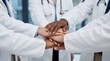 © FreemiumStock - Medical team stacking hands together in unity circle, diverse healthcare professionals in white lab coats showing solidarity