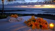 © StasySin - A table with two white towels and a vase of flowers with a candle in front of it. The table is set up on a beach, with the ocean in the background. The candles are lit, creating a warm
