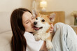 © st.kolesnikov - Young woman cuddling corgi dog while relaxing on sofa indoors