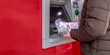 © Alina - Man is at an ATM withdrawing cash. He hold a bundle of turkish lira banknotes wrapped in a protective sheet. The machine displays a bright red exterior