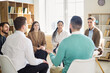 © Studio Romantic - People group of adults in team training meeting. A coach leads discussion with participants in a bright circle, sharing ideas and building skills. Concept of unity and open communication.