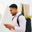 © Lumos sp - Portrait of a young businessman man using a smartphone mobile phone walking down the street, surrounded by moder corporate office buildings and modern city architecture