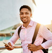 © Lumos sp - Portrait of a young businessman man using a smartphone mobile phone walking down the street, surrounded by moder corporate office buildings and modern city architecture