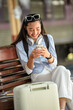 © arjan_ard_studio - Smiling Young Woman Using Smartphone While Waiting for Train