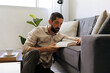 © kleberpicui - Adult man relaxing on sofa reading book at home with coffee nearby. Calm lifestyle moment representing mindfulness, rest and slow living in modern bright interior.