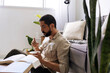 © kleberpicui - Adult man enjoying coffee while reading book at home. Quiet break moment highlighting relaxation, focus and balanced lifestyle inside bright modern living room.
