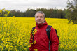 © Alexander - Aduld caucasian man wearing red jacket in bright yellow rapeseed field, enjoying spring outdoors. Concept of nature, healthy lifestyle, happiness, and well being.