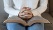 © kieferpix - close up of woman praying with hands clasped over open bible at home, christian faith and devotion