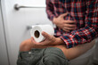 © kieferpix - Man with Stomach Pain Sitting on Toilet Holding Toilet Paper – Digestive Health Concept