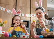 © Konstantin Yuganov - Mother and Daughter Painting Easter Eggs with Bunny Ears for Holiday Celebration