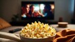 © mila103 - Cozy movie night at home with popcorn and tv in background.