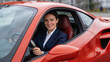 © ArtShop - Young woman smiling while driving a red sports car outdoors