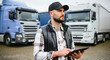 © Polina - Transport manager checking logistics on tablet, serious expression, trucks in background