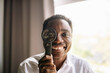 © yaaaaan - A cheerful black man smiles brightly while holding a magnifying glass up to his eye, immersed in curiosity.