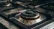 © MUHAMMAD - Dirty gas stove burner with grime and water droplets on a kitchen counter viewed from above closely.