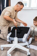 © Aboltin - Father assembling ergonomic office chair at home with son nearby. Creating comfortable workspace, home office setup, family involvement and modern lifestyle indoors