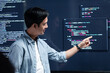 © SAT65 - Asian Male developer leading a team meeting, pointing to code on a big monitor while reviewing an AI chatbot module. Concept of collaboration, debugging for coding teamwork in a tech company office.