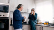 © DMegias - Elderly couple relaxing in pajamas, drinking coffee and talking in their modern kitchen, symbolizing domestic life and retirement