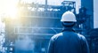 © MUHAMMADESHA - Industrial worker in hard hat standing in front of large industrial structure