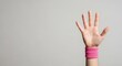 © Abuloy - A raised hand wearing a pink wristband against a plain background, symbolizing support and unity in fitness.