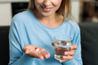 © brizmaker - Young woman takes medication with water in her home kitchen