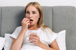 © brizmaker - Woman takes medicine with water while lying in bed at home in the morning