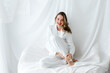 © Tania Cervian/Stocksy - Young woman wearing white suit smiling and relaxing on white sheets