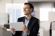 © fizkes - Smiling Hispanic office worker corporate employee holding digital tablet at workplace enjoying good news from marketing report satisfied with project success reviewing positive client feedback online