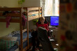© Viktar - teen boy sitting at desk beside bunkbed, blue screen glow and dim room creating atmospheric gaming or study session, relaxed posture and immersive digital focus