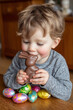 © Duckai - Kid eating Chocolate Easter Bunny holding bright painted eggs during cozy family spring holiday