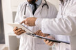 © fizkes - Digital and paper tools in medicine. Close up two male doctors medical workers in white coats discuss patient information analyze files on electronic tablet review written case history on clipboard