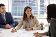 © fizkes - Professional middle-aged woman in formal attire sits at conference table with business partners, exude confidence, holds pen, ready to sign contract or agreement paper. Merger, commercial deal making