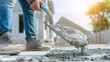 © dmmarychev - Construction worker in boots using shovel to spread wet concrete on building site