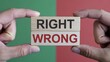 © Mudassir - Fingers carefully hold wooden blocks displaying the words right and wrong stacked vertically against a contrasting red and green background symbolizing choice