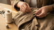 © RISHAD - Close up of hands sewing wooden button onto linen garment
