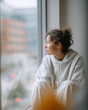 © lashkhidzetim - A woman sits in a window with her head down. She is wearing a gray hoodie and white pants