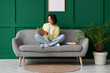 © Pixel-Shot - Pretty young woman reading book on sofa near green wall