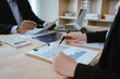 © Witoon - Two business people are discussing and analyzing financial charts and reports at their desks in an office, with laptops nearby. The atmosphere is serious and professional.