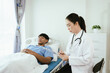 © Witoon - Female doctor reviewing medical records on a clipboard while a male patient rests in a hospital bed during inpatient care.
