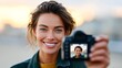 © Nataliia_Trushchenko - Smiling woman with wavy brown hair holds a camera in front of her face, capturing a selfie against a blurred outdoor background during sunset